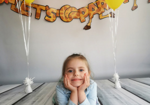 Dziewczynka leży na tle fotograficznym i pozuje do zdjęcia wśród balonów.